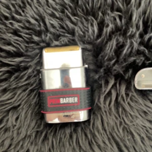 Babyliss elektrisk rakapparat - Säljer en elektrisk rakapparat från PRO BARBER i silverfärg med svart och rött grepp. Rakhuvudet är guldigt och apparaten har en kompakt, rektangulär form. Perfekt för en nära rakning och enkel att ta med sig.