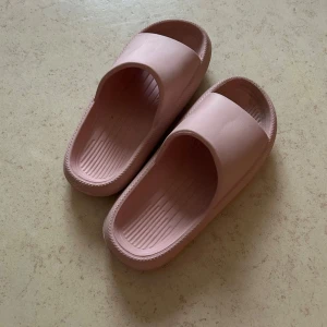 Rosa sandaler i syntetmaterial - Säljer ett par ljusrosa sandaler i syntetmaterial. De har en enkel och stilren design med öppen tå och räfflad sula för extra komfort. Perfekta för sommaren eller att ha hemma.