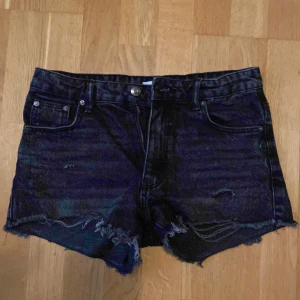 Svarta jeansshorts från Gina Tricot - Snygga svarta jeansshorts från Gina Tricot med slitna detaljer och fransig kant nedtill. Klassisk femficksmodell och knappgylf. Perfekta för en avslappnad stil.