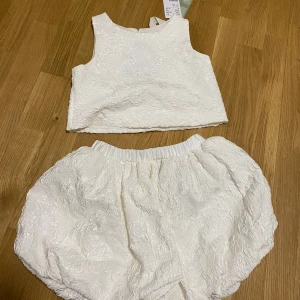 Vit croppad linnetopp med strukturmönster - Säljer en vit croppad linnetopp från H&M med vacker struktur i tyget. Toppen är ärmlös och har en rund halsringning. Perfekt för sommarens varma dagar och passar till både kjol och byxor.