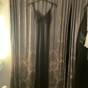 Svart långklänning med spetsdetaljer - Supersnygg svart långklänning från Bubbelroom med tunna axelband och v-ringning. Klänningen har spetsdetaljer vid bysten och öppen rygg med justerbara band. Perfekt för dig som vill ha en elegant och stilren look.