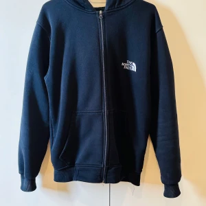 Svart hoodie från The North Face Summit Series - Säljer en svart hoodie från The North Face Summit Series med dragkedja och huva. Tröjan har två fickor framtill och logga på bröstet. Perfekt för dig som gillar enkel och sportig stil.
