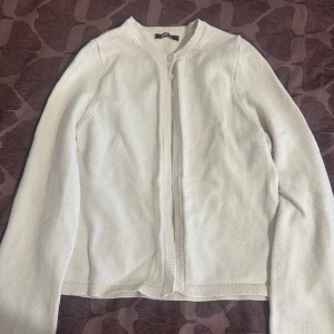 Vit kofta från Gina Tricot, storlek S - En stilren vit kofta från Gina Tricot i storlek S. Koftan har rund halsringning, ribbade kanter och stängs med en knapp upptill. Perfekt att slänga över en topp för en clean look. Materialet är mjukt och stickat för extra komfort.