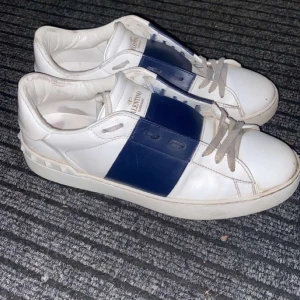 Valentino Garavani Open sneakers vit/marinblå - Snygga Valentino Garavani Open sneakers i vit och marinblå. Skorna ä i storlek 41. Skorna ä i ganska bra skick men har en liten skada på högra skon.