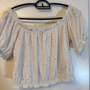 Vit offshoulder blus från Gina Tricot - Superfin vit blus från Gina Tricot med offshoulder-modell och korta puffärmar. Blusen har broderade hålmönster och volangdetaljer vid ärmslut och nederkant. Finns inga defekter. Pris kan diskuteras.