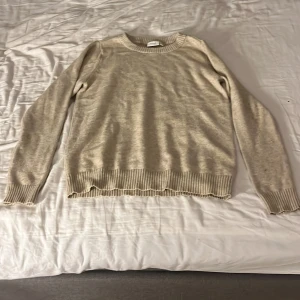 Beige stickad tröja med ribbade muddar - En stilren beige stickad tröja med rund halsringning och ribbade muddar vid ärmslut och nederkant. Tröjan har en klassisk passform. Säljer den för att den inte används längre  