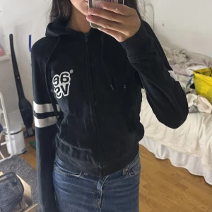 Svart hoodiejacka från Svea XS - Svart hoodiejacka från Svea med dragkedja, vita ränder på ärmarna och broderad logga på bröstet. Jackan har huva med snörning och en sportig vibe. Perfekt till jeans eller joggers för en chill look.