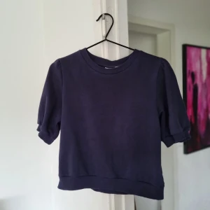 Mörkblå kortärmad tröja Gina Tricot - Mörkblå tröja från Gina Tricot med kort puffärm och ribbade muddar. Modellen är boxig och lite croppad, perfekt till jeans eller kjol. Mjuk och skön i bomullsmix, enkel att styla för en chill look.