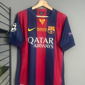 FC Barcelona Neymar Jr 2015 matchtröja - Barças officiella matchtröja från Champions League-finalen 2015 med Neymar Jr och nummer 11 på ryggen. Rödblåa vertikala ränder, gula detaljer och klubbmärke på bröstet. Qatar Airways-tryck fram, Unicef bak. Korta ärmar, lätt och ventilerande material. Helt ny med tagg en replika