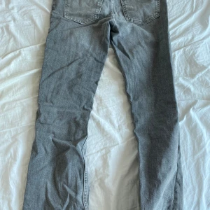 Grå jeans från Gina Tricot, storlek 164 - Säljer ett par grå jeans från Gina Tricot i storlek 164. Jeansen har bootcut, klassiska bakfickor och slitna detaljer på benen för en cool look. Tillverkade i bomull med en skön passform som funkar till många stilar.