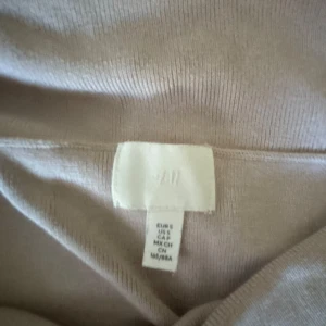 Beige offshoulder tubtopp från H&M - Säljer en beige offshoulder tubtopp från H&M i ribbat material. Toppen har en bred vikt kant upptill som ger en snygg och trendig look. Perfekt att styla med jeans eller kjol för en cool vibe.