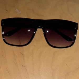 Helt nya Svarta solglasögon - Helt nya Stilrena svarta solglasögon med fyrkantig form och mörka tonade glas. Perfekta för att ge en cool vibe till din outfit och skydda ögonen mot solen. Passar dig som gillar en klassisk men trendig look.