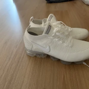 Nike Vapormax vita sneakers strl 43 - Nike Vapormax sneakers i helvitt med stickad ovandel och transparent sula. Skorna har snörning och en modern, sportig look. Perfekta för dig som gillar stilrena och lätta sneakers med maximal komfort. PRISET KAN DISKUTERAS 