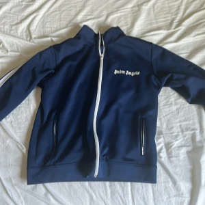 Blå track jacket från Palm Angels M - Snygg blå track jacket från Palm Angels med vit dragkedja och logga på bröstet. Jackan har långa ärmar med vita ränder längs sidorna och två fickor framtill.