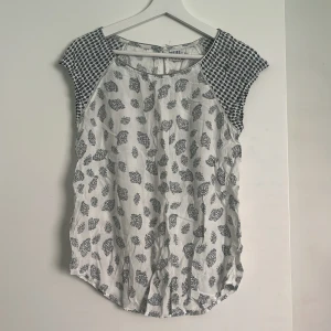 Vit blommig blus från Saint Tropez - Supersöt vit blus från Saint Tropez i storlek XS. Toppen har gråblått blommönster på framsidan och coolt grafiskt mönster på axlarna. Lätt och luftig med rund hals och korta ärmar, perfekt för en fräsch och chill look.