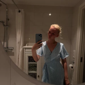 Ljusblå omlottklänning med leopardmönster - Superfin ljusblå kort omlottklänning med vitt leopardmönster och knyt i midjan. Klänningen har v-ringning och korta ärmar, perfekt för en fräsch och trendig look. Materialet känns lätt och svalt, perfekt för varmare dagar. Nypris 439kr