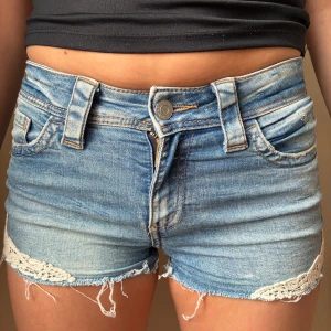 Blå lågmidjade jeansshorts  - Snygga ljusblå jeansshorts från H&M med fransiga benslut och vit spetsdetalj längs kanterna. Shortsen är väldigt stora i storleken. Säljer på grund av att det är för små. Pris kan diskuteras!❤️