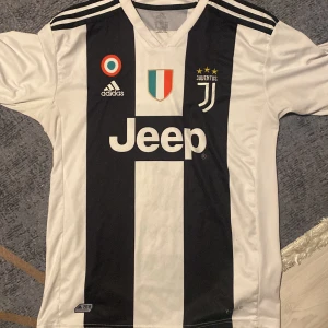 Juventus Ronaldo 7 matchtröja Adidas XL - Juventus hemmatröja från Adidas i storlek XL med Ronaldo 7 på ryggen. Klassisk svartvit randig design, broderade klubbmärken och sponsortryck. Tillverkad i lätt och ventilerande polyester med Climalite-teknologi. Perfekt för dig som älskar fotboll och Juventus.
