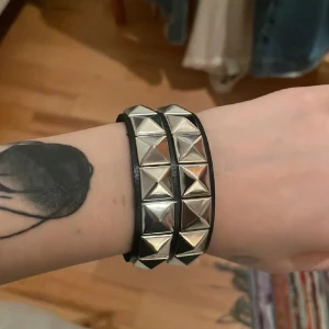 Svart läderarmband med nitar - Coolt svart armband i läder med stora silvriga pyramidnitar runt om. Perfekt accessoar för dig som gillar en edgy och alternativ stil. Armbandet är brett och ger en riktigt tuff känsla till din outfit.