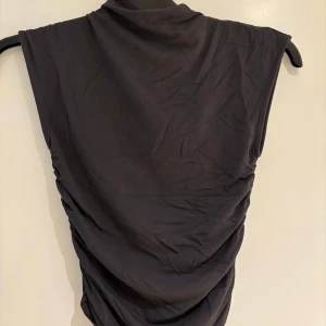 Svart ärmlös topp från Gina Tricot - Säljer en svart ärmlös topp från Gina Tricot i storlek XS. Toppen har en enkel och stilren design med lätt rynkade sidor som ger en snygg siluett. Perfekt att matcha med jeans eller kjol för en trendig look.