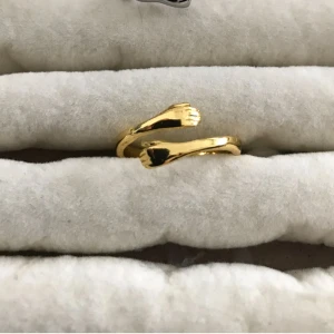 Rostfritt stål ring  - Unik guldfärgad ring med två händer som möts framtill och skapar en cool och personlig look. Ringen har en öppen design och glänsande finish som verkligen sticker ut. Perfekt för dig som vill ha ett smycke med lite edge och känsla.