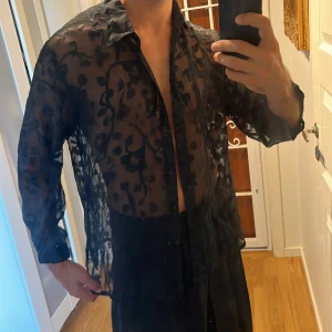 Svart transparent blommig skjorta - Säljer en svart transparent skjorta från Woodpecker Collection i storlek 40/42. Skjortan har ett blommigt mönster, klassisk krage och knäppning framtill. Perfekt för dig som vill sticka ut med en edgy och unik stil.