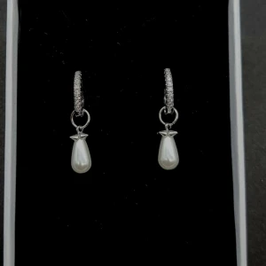 Silverörhängen med pärldroppar - Stilrena örhängen i silverfärg med gnistrande stenar på ringen och hängande droppformade vita pärlor. Detaljerad infattning upptill på pärlan ger en elegant touch. Perfekta för dig som gillar klassiska smycken med lite extra bling.