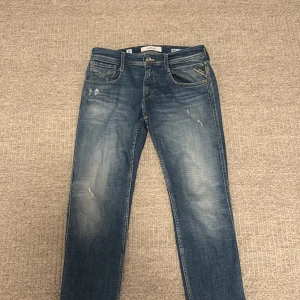 Replay Anbass - Säljer ett par Replay Anbass jeans i klassisk blå tvätt med slitningar och snyggt blekta partier. Jeansen har fem fickor, normal passform och raka ben. Märkesdetaljer på ficka och bak med Replay-lapp i läder. Perfekta för en avslappnad stil.