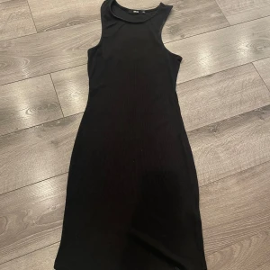 Svart ärmlös tight klänning från BIK BOK - Enkel och stilren svart klänning från BIK BOK. Modellen är tight, ärmlös och har en rund halsringning. Perfekt för dig som gillar minimalistisk stil och vill ha en klänning som sitter snyggt på kroppen.