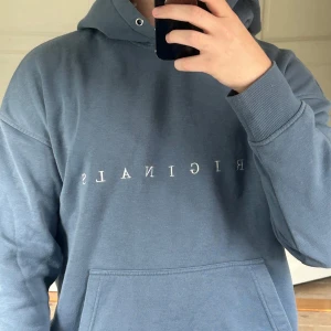 Blå hoodie från Jack&Jones - Snygg blå hoodie från Jack&Jones med vit text på bröstet. Tröjan har huva, magficka och ribbade muddar vid ärmslut och nederkant. Perfekt för chill dagar och enkel att matcha med jeans eller joggers. 