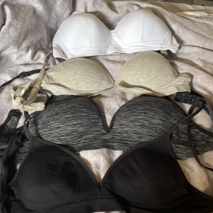 4-pack bandeau toppar i olika färger (70A) - Säljer fyra bandeau toppar i svart, gråmelerad, beige och vit. Alla har vadderade kupor och avtagbara axelband. Perfekta under en skjorta eller till en öppen rygg. Mjukt material och bekväm passform, passar dig som gillar enkel och clean stil.