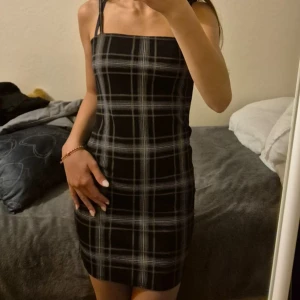 Rutig svart klänning från NLY Trend - Supersnygg kort rutig klänning från NLY Trend i svart med vita och grå rutor. Tight passform med smala axelband och rak halsringning. Perfekt för dig som gillar en stilren och trendig look.