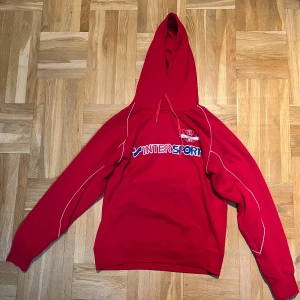 Röd hoodie Pro Touch x Intersport M - Röd hoodie från Pro Touch med stor Intersport-logga på bröstet och vita detaljer längs ärmarna. Klassisk känguruficka framtill, snörning i huvan och tryckt klubbmärke på bröstet. Perfekt för dig som gillar sportig stil.