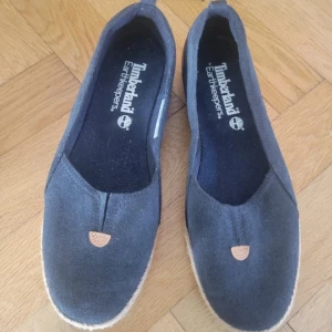 Mörkblå  Timberland skor - Snygga mörkblå skor från Timberland Earthkeepers med ovandel i mocka och beige detaljer i skinn. Sulan har flätad jutedetalj och vit undersida. Perfekta för vår och sommar, med rund tå och platt sula för en avslappnad look.