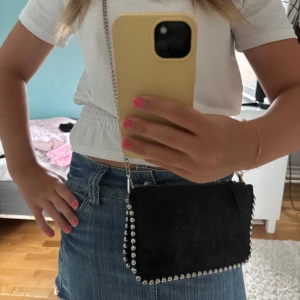 Svart axelväska med silverdetaljer - Snygg svart axelväska i mocka med silverfärgade nitar runt kanterna och kedjerem. Väskan har dragkedja upptill och flera fack inuti🥰💛 pris kan diskuteras och jag skickar så snabbt jag kan🥰🩷