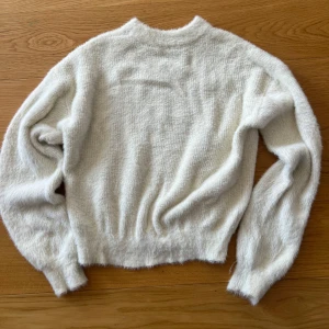 Vit fluffig stickad tröja - Supermjuk och fluffig vit stickad tröja med lång ärm och rund hals. Perfekt för dig som gillar en cozy vibe och vill ha något riktigt gosigt till kyliga dagar. Tröjan har en enkel design och är lätt att matcha med jeans eller kjol.
