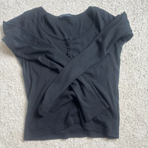 Topp brandy Melville - Svart långärmad topp från Brandy Melville med rund halsringning och tre knappar framtill. Tillverkad i mjuk bomull med en slim passform. Perfekt att styla med jeans eller kjol för en enkel och clean look. Helt ny och aldrig anvönd❤️