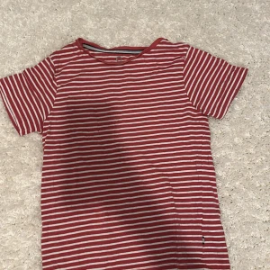 Rödvit randig t-shirt från C - Snygg t-shirt i röd och vit med klassiskt randigt mönster från C. Tillverkad i mjuk ekologisk bomull, perfekt för en chill och stilren look. Kortärmad modell med rund halsringning och relaxed fit.