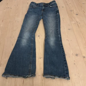 Blå bootcut jeans med slitningar - Snygga blå jeans med bootcut passform och slitna detaljer vid bensluten. Jeansen har klassisk femficksdesign, dragkedja och knapp framtill. Materialet är robust denim i bomull och färgen har en schysst tvättad look med ljusare partier. Bra skick💗