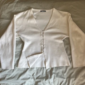 Vit tröja med knappar från Gina Tricot - Säljer en stilren vit kofta från Gina Tricot i storlek M. Koftan har v-ringning, långa ärmar och snygga tygklädda knappar framtill. Materialet är mjukt och stickat, perfekt för lager-på-lager. Enkel och clean design som funkar till allt.