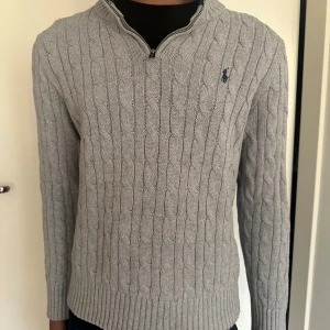 Grå stickad tröja Polo Ralph Lauren - Grå kabelstickad tröja från Polo Ralph Lauren i storlek 10-12 vilket motsvarar ungefär 150-160 cm. Tröjan är i fint skick. Kontakta vid funderingar.💯👌
