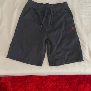 Mörkblå shorts från Polo Ralph Lauren - Snygga mörkblå shorts från Polo Ralph Lauren med röd broderad logga på benet. Modellen har elastisk midja med snörning och två sidofickor. Perfekta för sommaren och riktigt sköna tack vare mjukt bomullsmaterial.