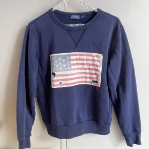 Blå sweatshirt Polo Ralph Lauren - Mörkblå sweatshirt från Polo Ralph Lauren. Använd men har inga defekter förutom slitningar på flaggan. Nytvättad.  Storlek xs.