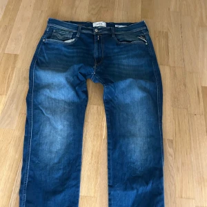 Replay Hyperflex blå jeans W36 L32 - Snygga Replay Hyperflex jeans i klassisk blå tvätt med lätt slitning och raka ben. Jeansen har fem fickor, kontrastsömmar och läderpatch bak i midjan. Stretchigt material för extra komfort och cool passform. De är små slitningar vid skrevet som går att fixa med att sy. Skicka om du har funderingar 