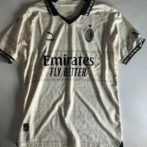 AC Milan x Puma beige fotbollströja M - AC Milan fotbollströja från Puma i beige med svarta detaljer och subtila grafiska mönster. korta ärmar med svart mönstrad kant och tryckta loggor. Tillverkad i lätt och ventilerande polyester, perfekt för match eller träning eller bara till vardags inga täcken på användning, ny pris runt 1100 har kvitto osv 