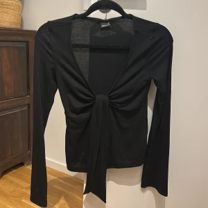 Svart långärmad knytblus Gina Tricot - Svart långärmad topp från Gina Tricot med djup v-ringning och snygg knytning framtill. Aldrig använd!!!