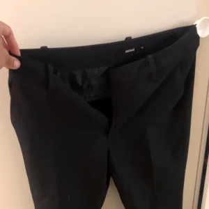 Svarta kostymbyxor från BikBok - Svarta kostymbyxor från BikBok utsvängda kostymbyxor med slits längst ner! 