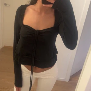 Svart långärmad topp med snörning - Trendig svart långärmad topp med fyrkantig urringning och snygg snörning framtill. Modellen är croppad och har en figurnära passform som framhäver midjan. Perfekt för dig som gillar stilrena och coola plagg med en twist.