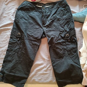 Svarta cargopants från Esprit - Svarta cargopants från Esprit med flera fickor och coola detaljer som knappar och öljetter. Byxorna är croppade och har en avslappnad passform, perfekta för en chill och streetig look. Tillverkade i bomull för skön känsla hela dagen.