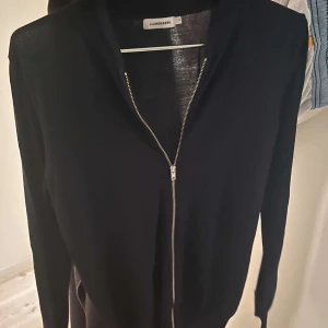 Marinblå cardigan från J.Lindeberg - Svart cardigan jacka från J.Lindeberg med stilren design och hel dragkedja framtill. Jackan är långärmad och tillverkad i ett tunt, stickat material som passar perfekt för lager-på-lager. Enkel och clean look som funkar till många outfits.